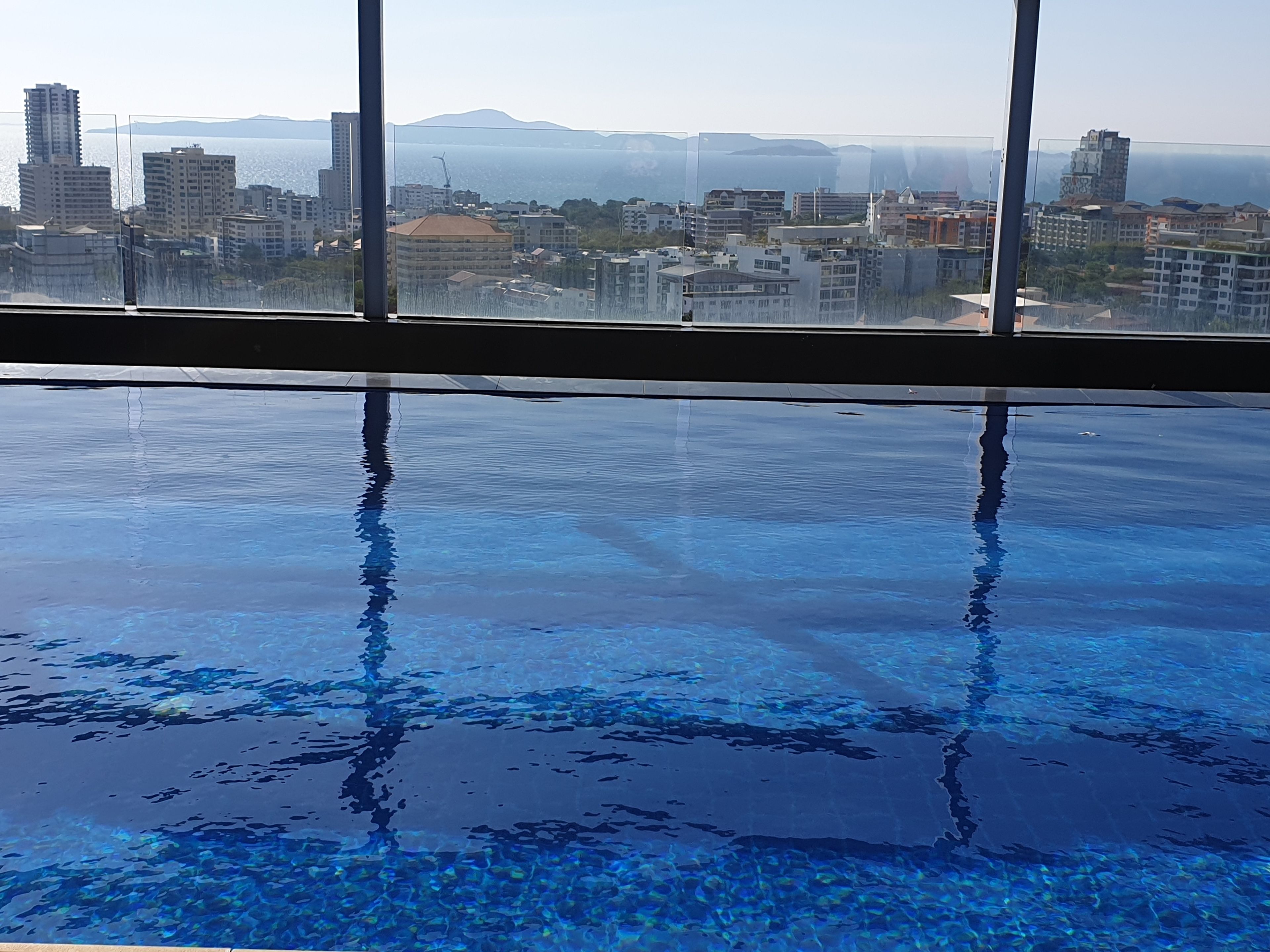 An indoor swimming pool with clear water and reflections of buildings and mountains in the background.