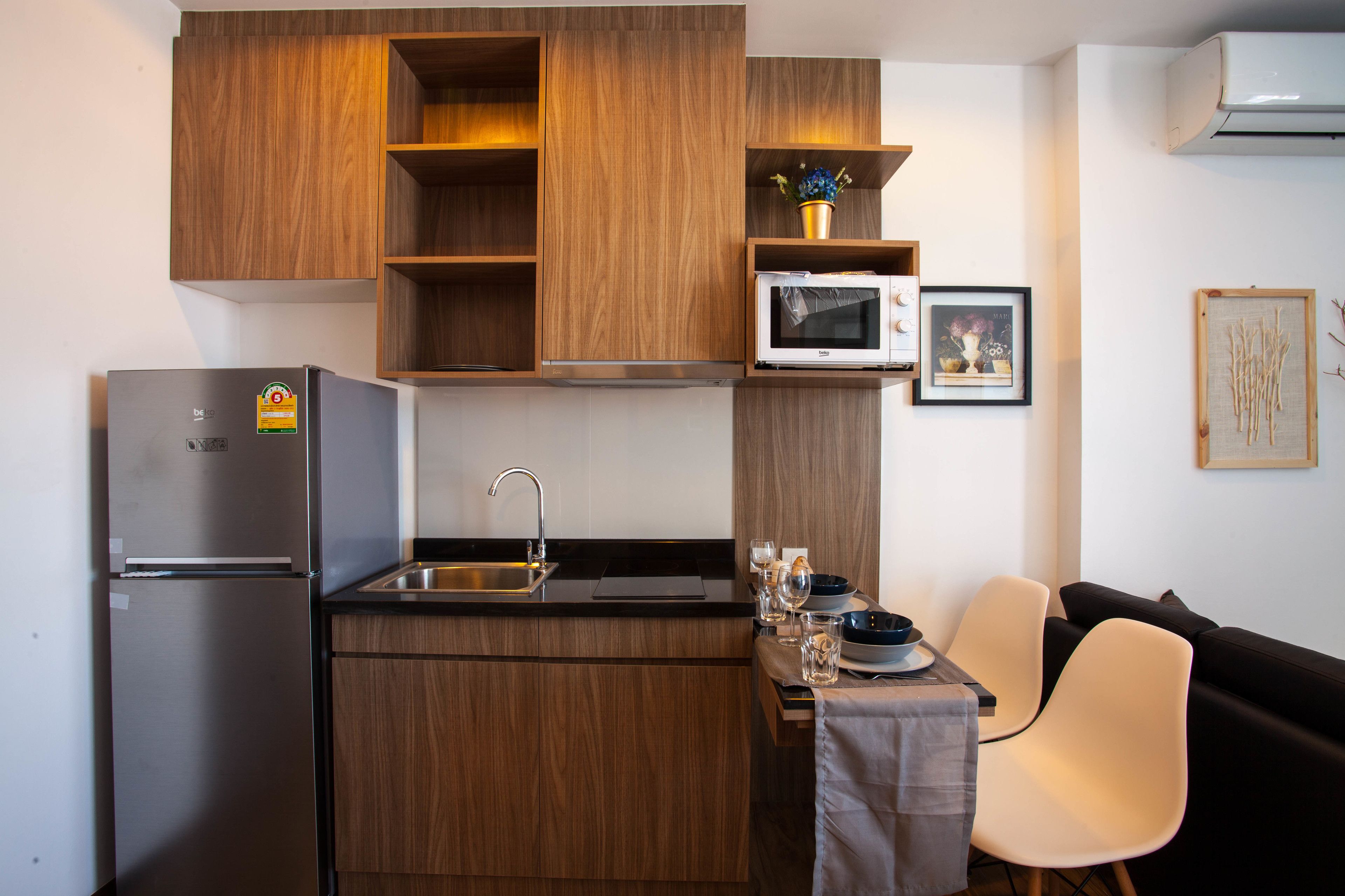 Eine kompakte Küche mit Holzausstattung, einem Edelstahlkühlschrank, einer Mikrowelle und einem Essbereich mit Tisch und Stühlen.