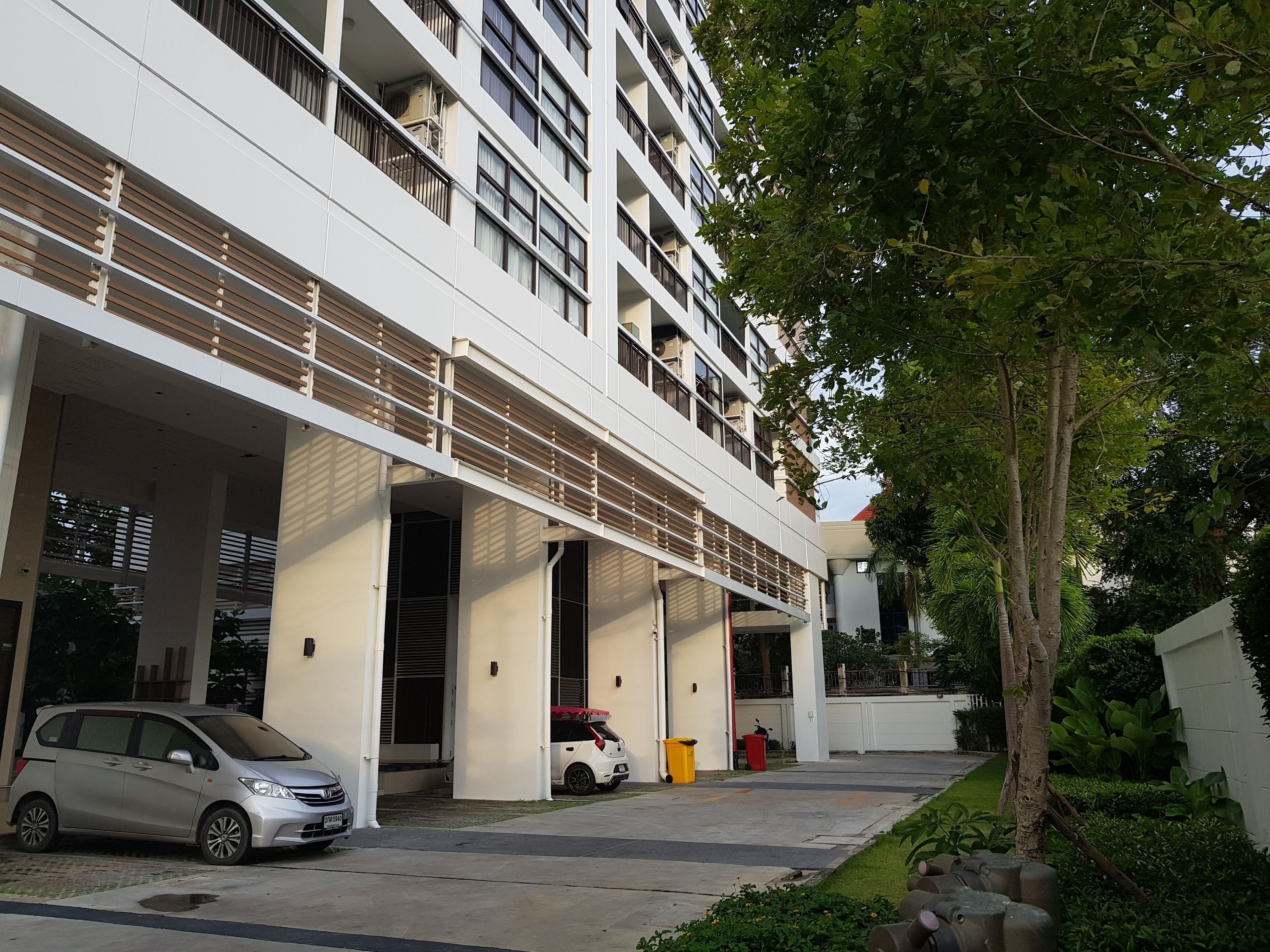 A multi-story building with a covered parking area, a tree, and a small garden area.