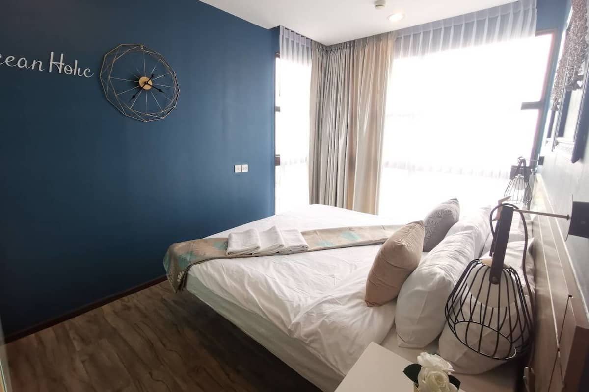 A bedroom with a bed, a wall clock, and a window with curtains.