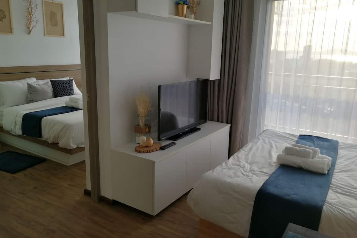 A modern hotel room with a bed, a TV on a white console, and a window with curtains.