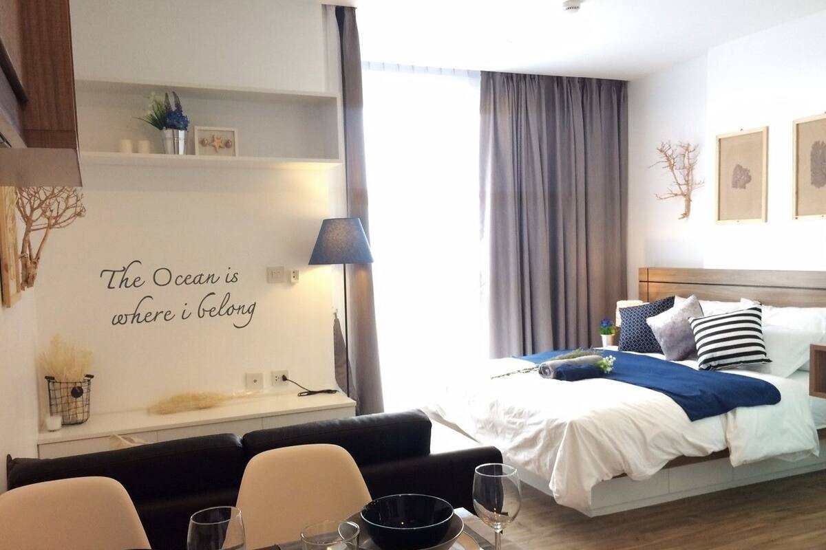 A hotel room with a bed, a desk with a lamp, a dining area with chairs and a table, and a wall with a decorative quote.