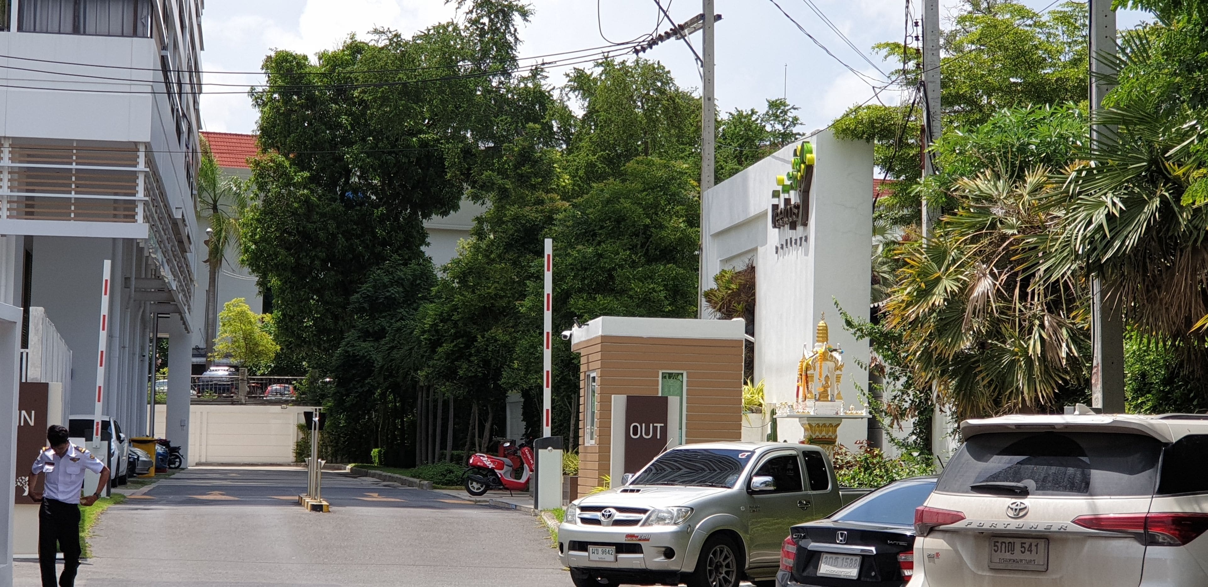 Una calle con coches aparcados, un edificio con un cartel que dice 'OUT' y una estatua.