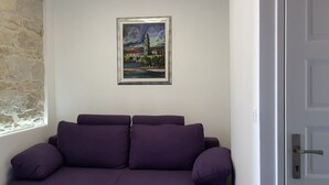 Ein Zimmer mit einem violetten Sofa, einem gerahmten Stadtbild und einer Steinwand.