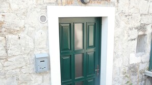 Eine grüne Tür mit weißem Rahmen, darüber ein kleines Fenster und rechts daneben ein Blumentopf.