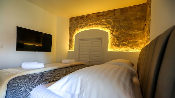 Ein Hotelzimmer mit steinernen Rundbögen, einem an der Wand befestigten Flachbildfernseher, einem Bett mit weißen Leinen und einer gemusterten Tagesdecke.