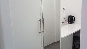 Ein Zimmer mit einem weißen Kleiderschrank, einem weißen Schreibtisch und einem schwarzen Wasserkocher.