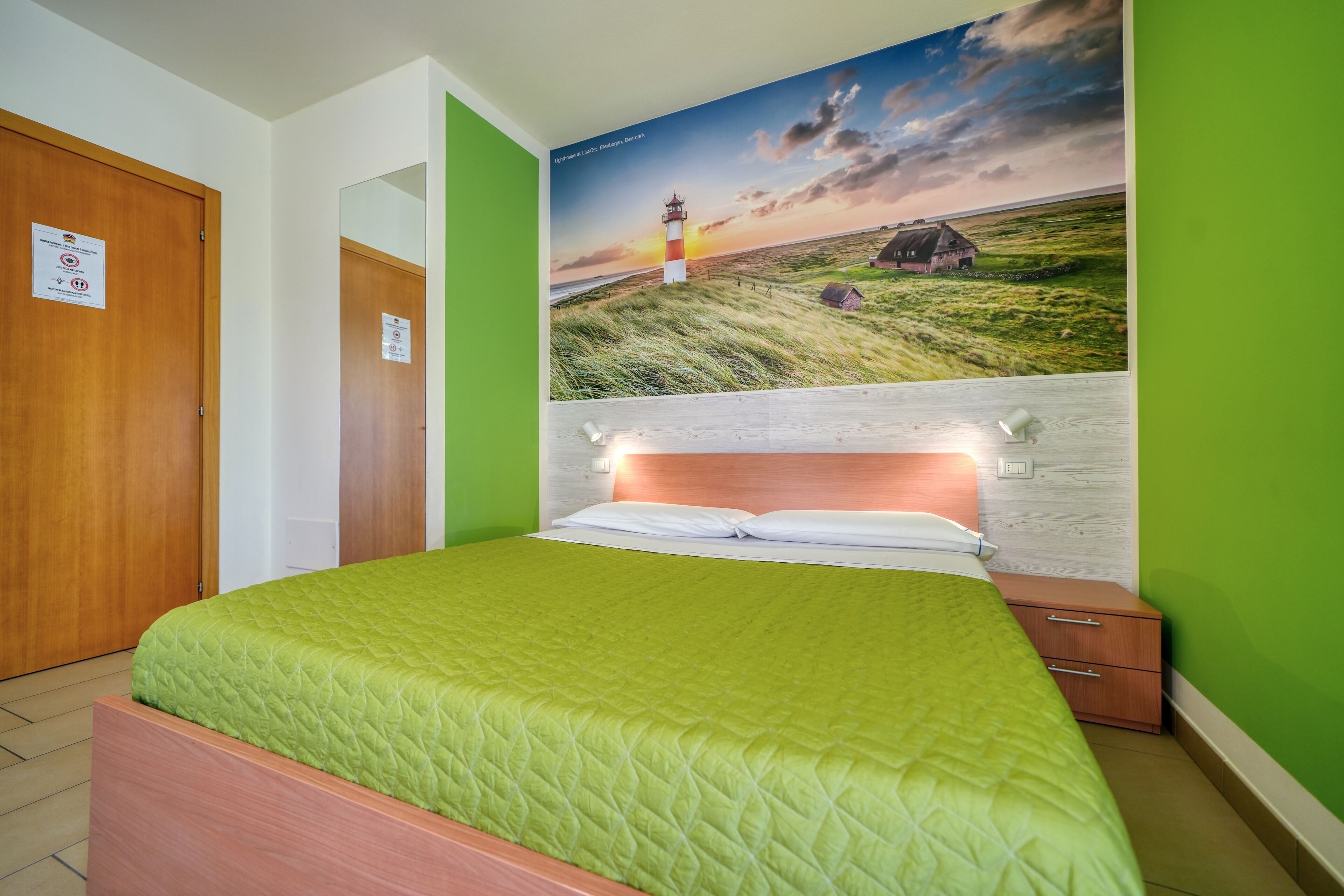 Une chambre à coucher avec une couvre-lit verte, une tête de lit en bois, une table de chevet et une lampe fixée au mur.