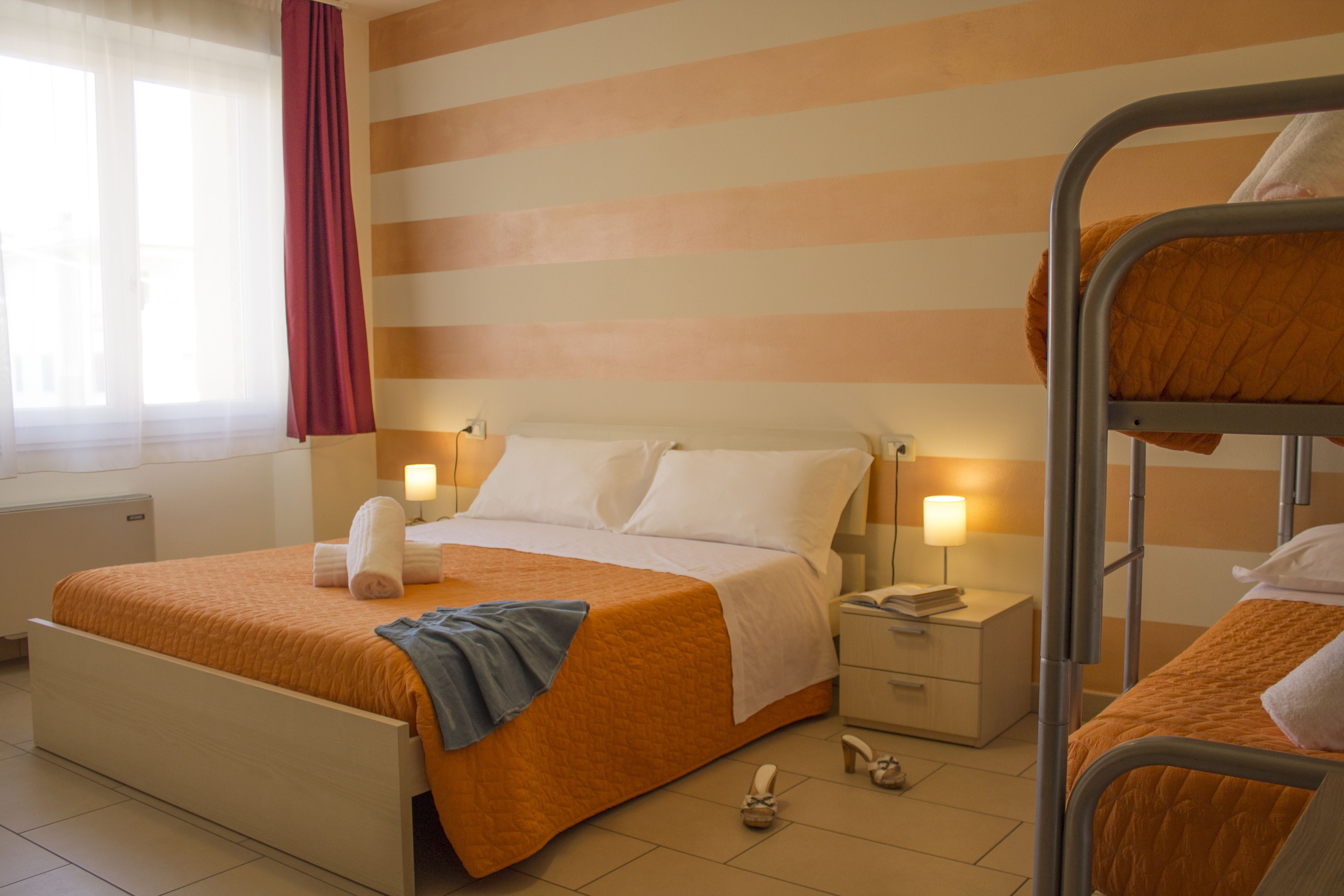 A hotel room with a single bed, a bunk bed, a nightstand, a lamp, and a window with curtains.
