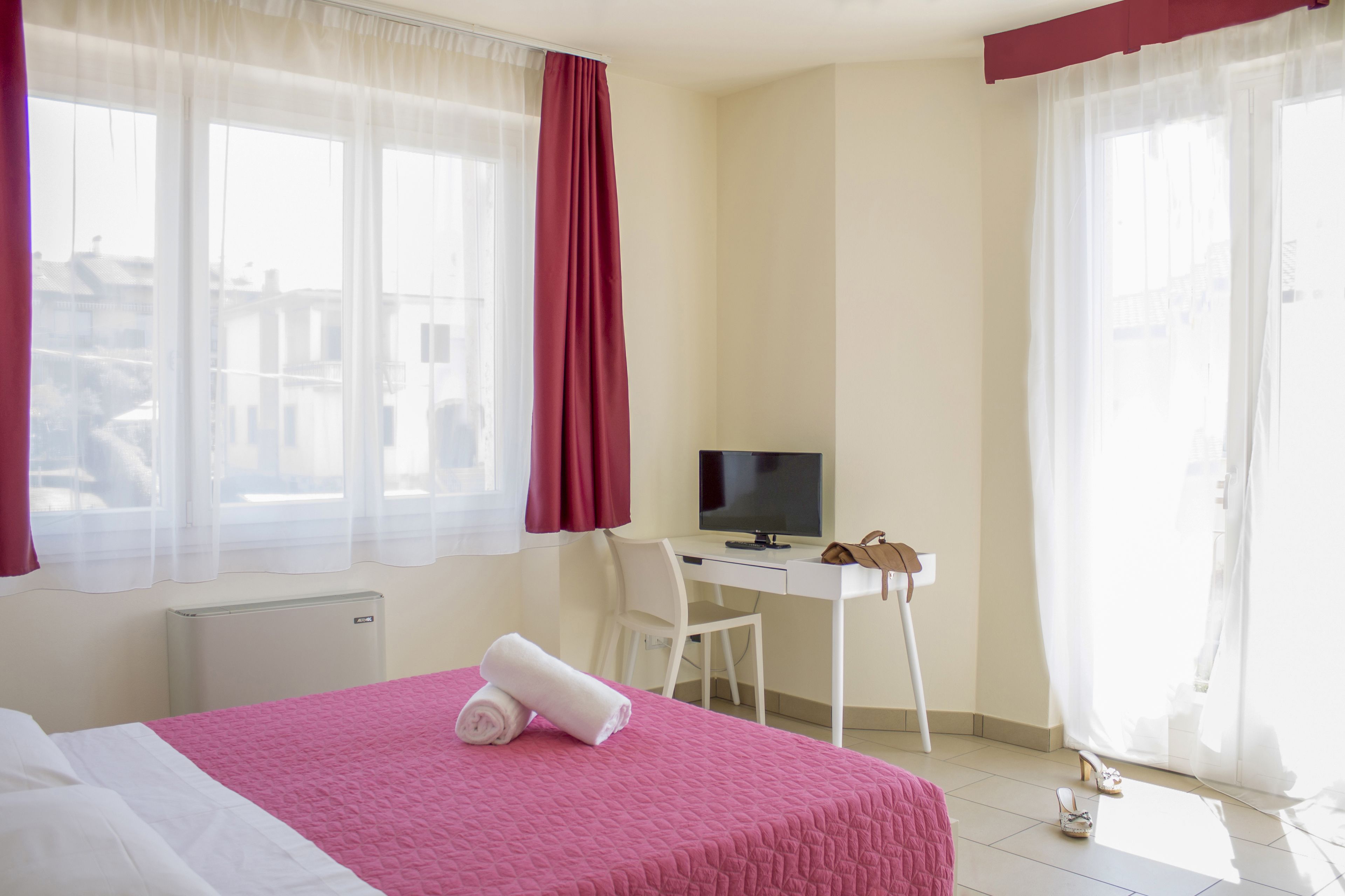 Ein Hotelzimmer mit Bett, Schreibtisch, Stuhl, Fernseher und einem Fenster mit Vorhängen.