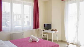 Ein Hotelzimmer mit Bett, Schreibtisch, Stuhl, Fernseher und einem Fenster mit Vorhängen.
