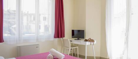 A hotel room with a bed, a desk, a chair, a TV, and a window with curtains.