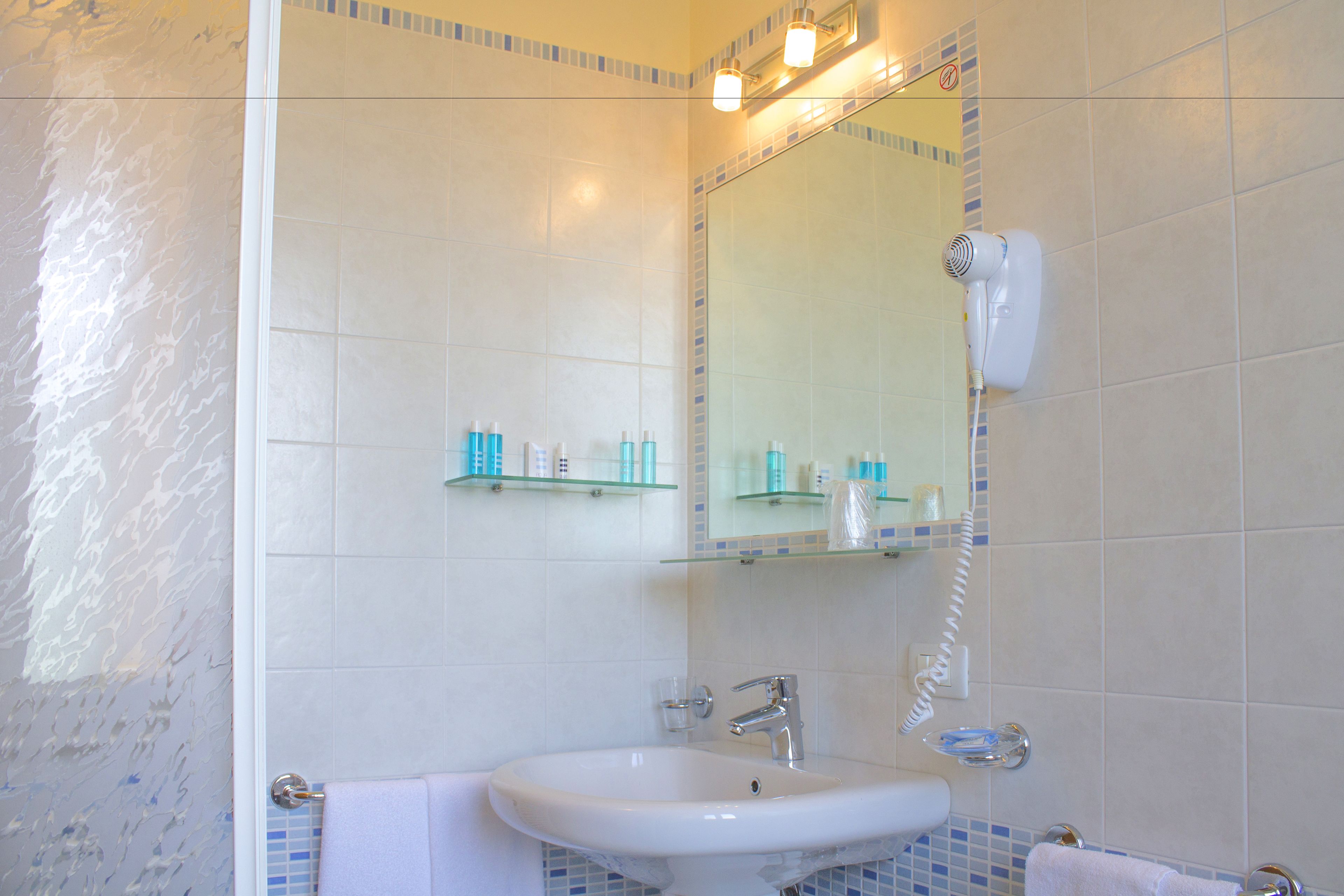 Ein Badezimmer mit einem weißen Waschbecken, einem Spiegel und einem an der Wand befestigten Föhn.