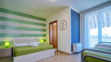 A hotel room with a bed, a nightstand, a lamp, a radiator, and a window with curtains.