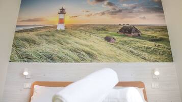 Ein Schlafzimmer mit einem Bett, einer Wandleuchte und einem Gemälde von einem Leuchtturm und einer Landschaft.