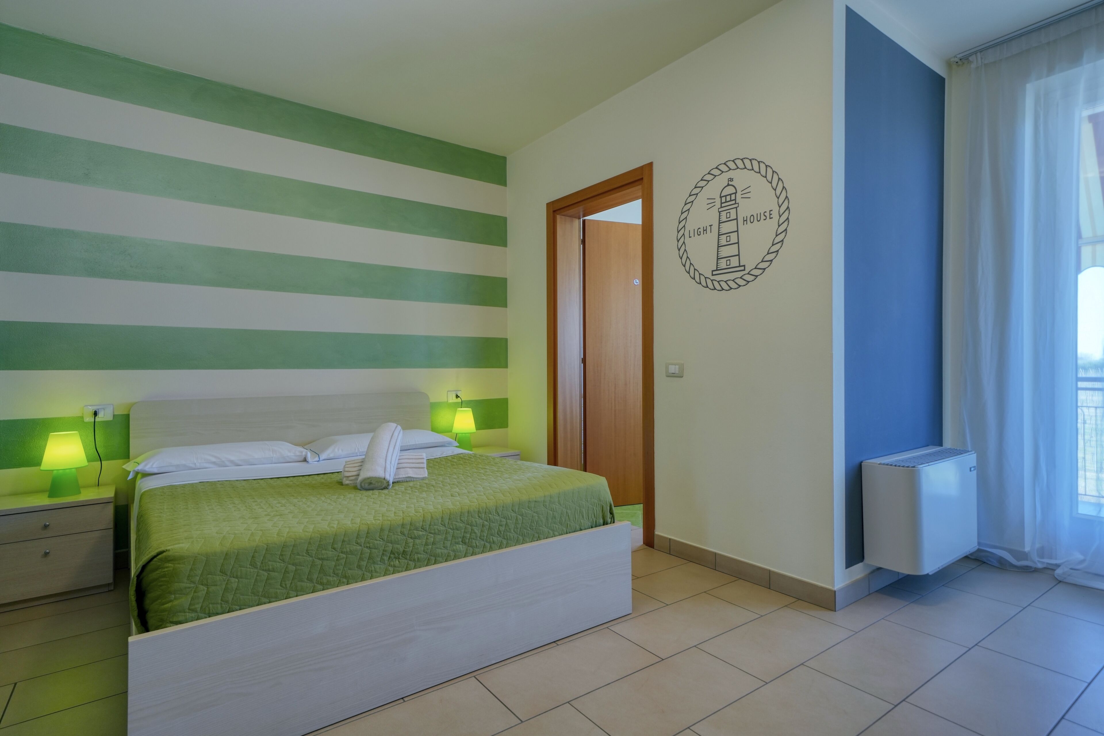 A hotel room with a bed, nightstands, a wall clock, a radiator, and a window with curtains.