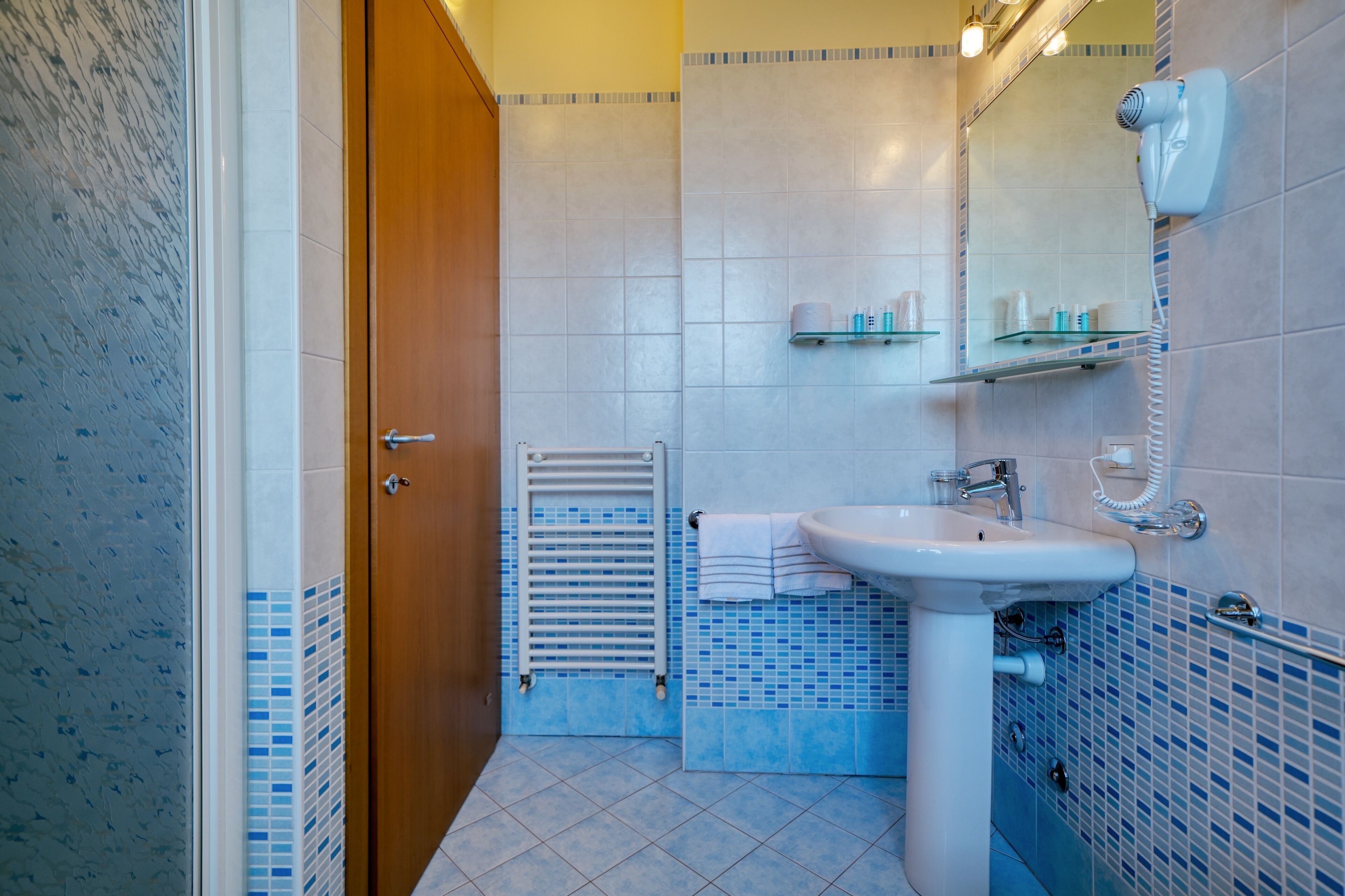 A bathroom with a white sink, a mirror, and a hairdryer mounted on the wall.