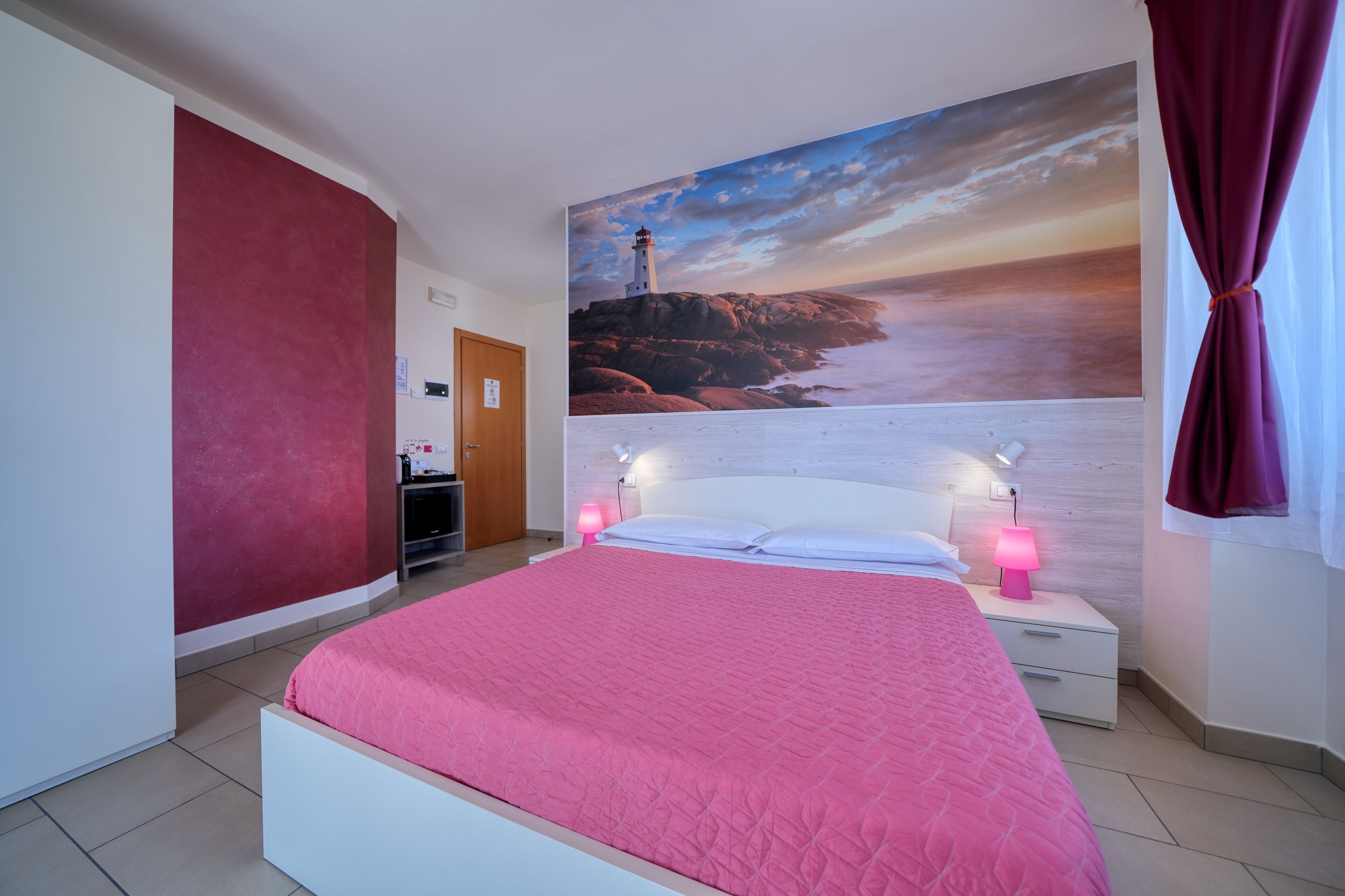 Une chambre à coucher avec un grand lit, une table de chevet avec une lampe, un téléviseur fixé au mur et un tableau représentant un phare.