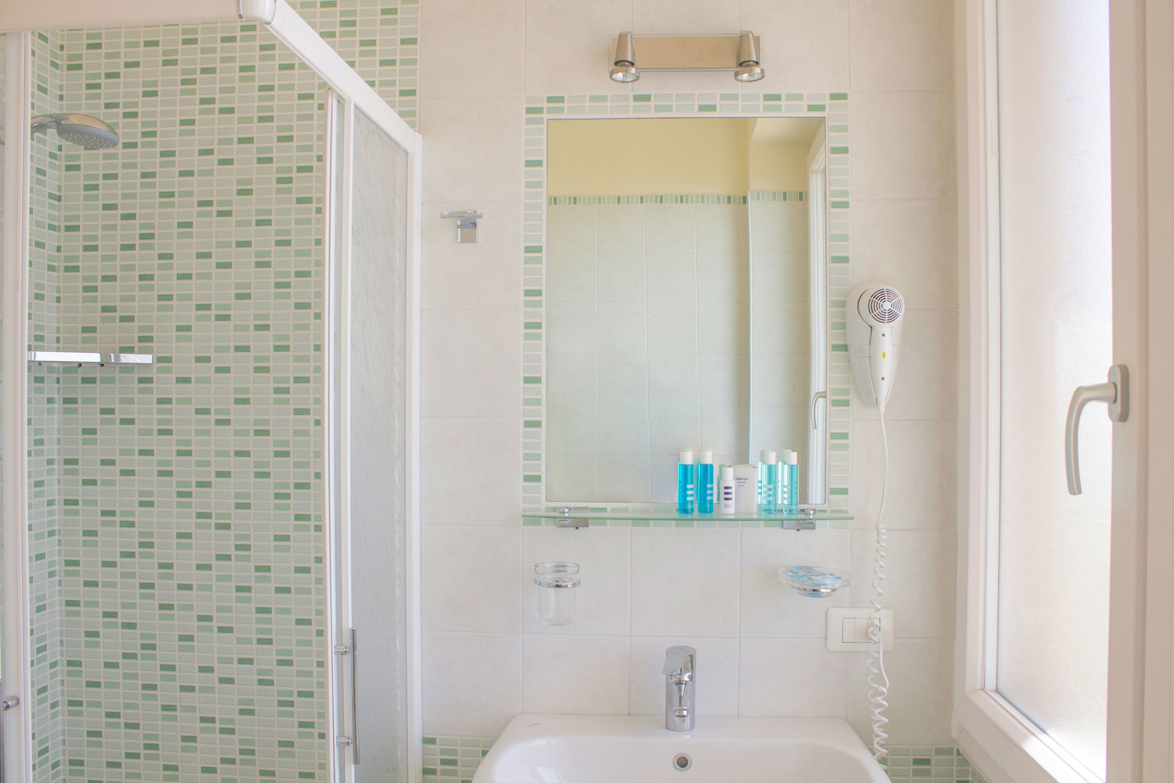 Un baño con ducha, lavabo, espejo y secador de pelo.