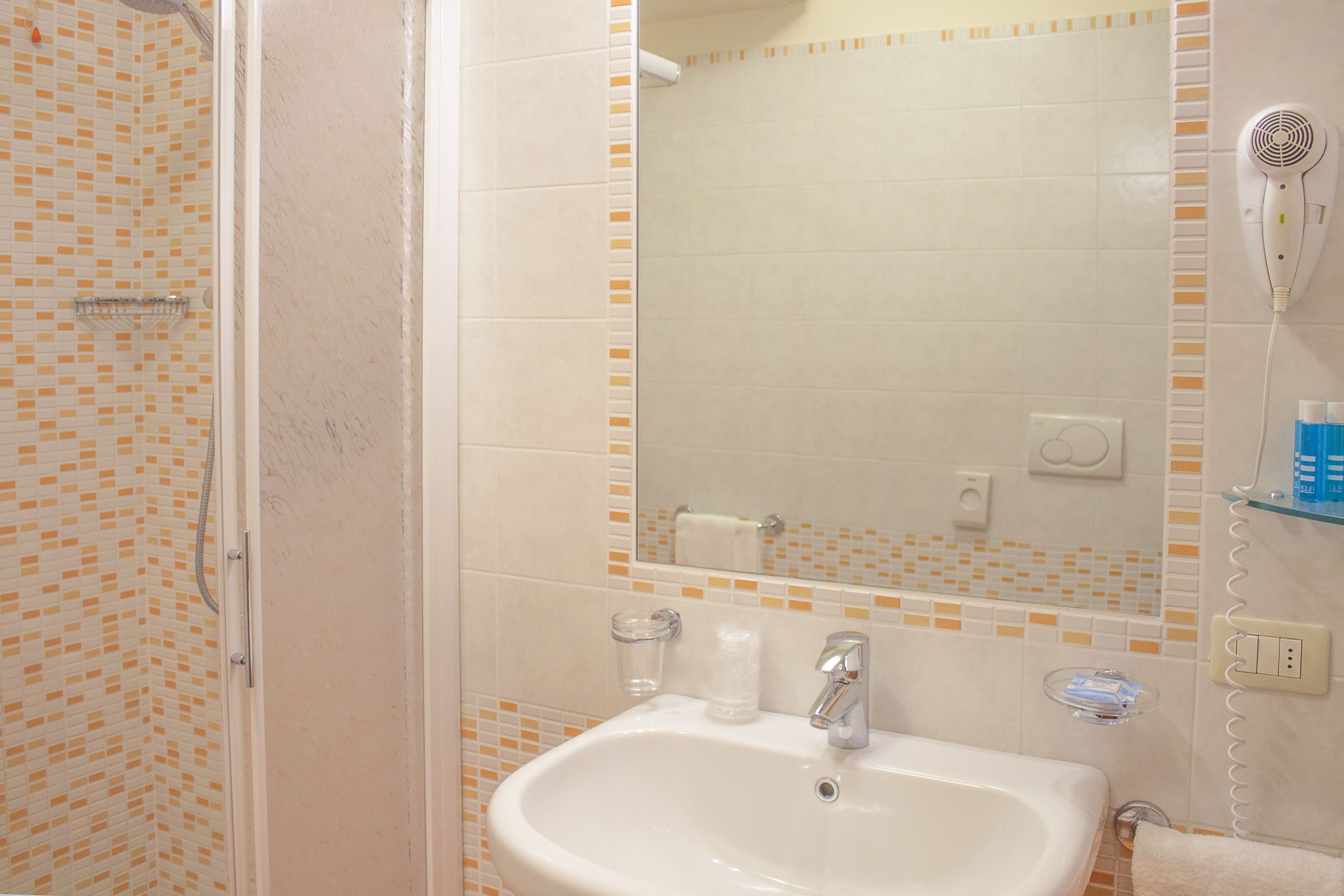 A bathroom with a shower, sink, and a hairdryer on a wall-mounted shelf.