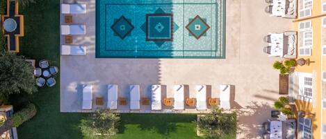 Vista aérea de un complejo turístico con piscina, tumbonas y zonas de estar al aire libre.