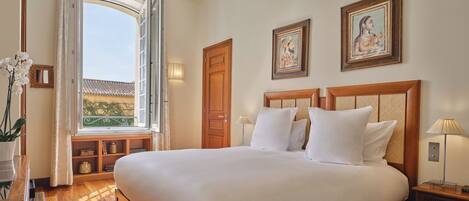 A well-lit bedroom with a large bed, wooden headboard, and two framed pictures on the wall.