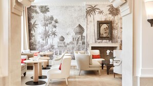 A modern lounge area with sofas, round tables, and a mural of a tropical landscape. - Airelles Pan Dei Palais (Saint-Tropez)
