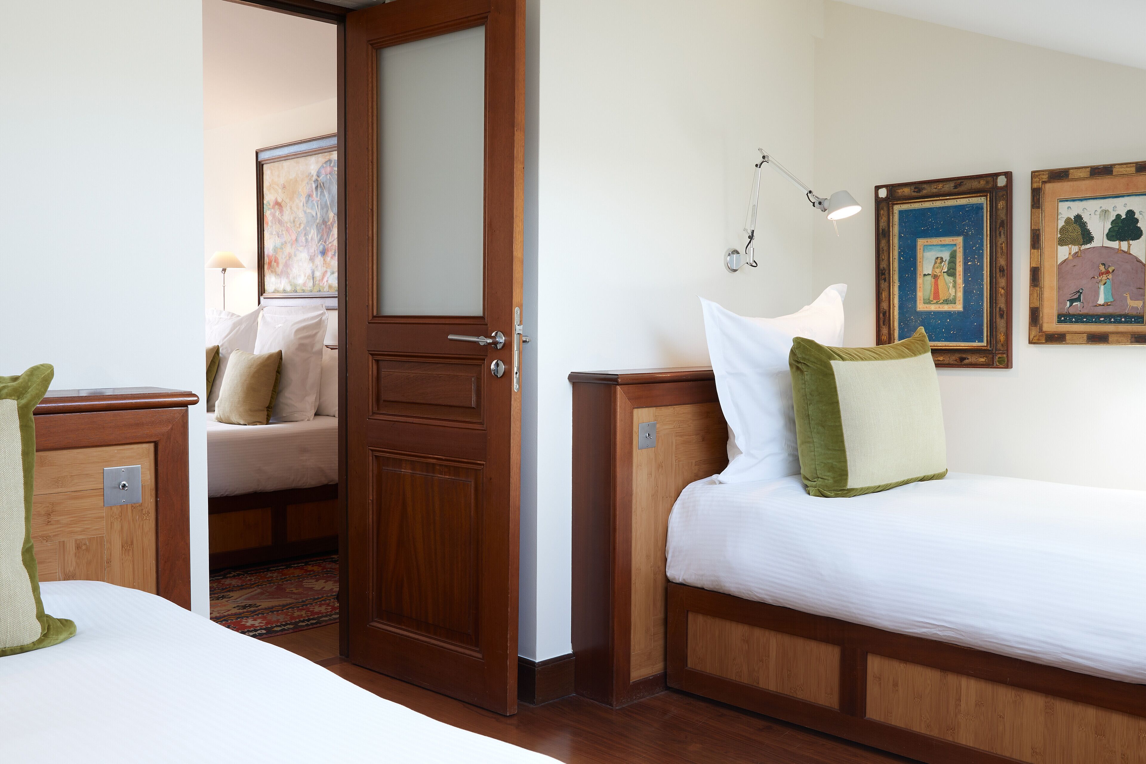 A hotel room with a wooden door, a bed with white bedding, a nightstand, a lamp, and two framed pictures on the wall.