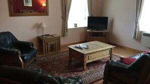 Un salon avec un téléviseur, des fauteuils en cuir, une table basse et un tapis à motifs.