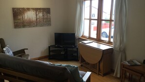 Una habitación acogedora con una cama de madera, un escritorio con silla, un televisor y un amplio ventanal con cortinas.