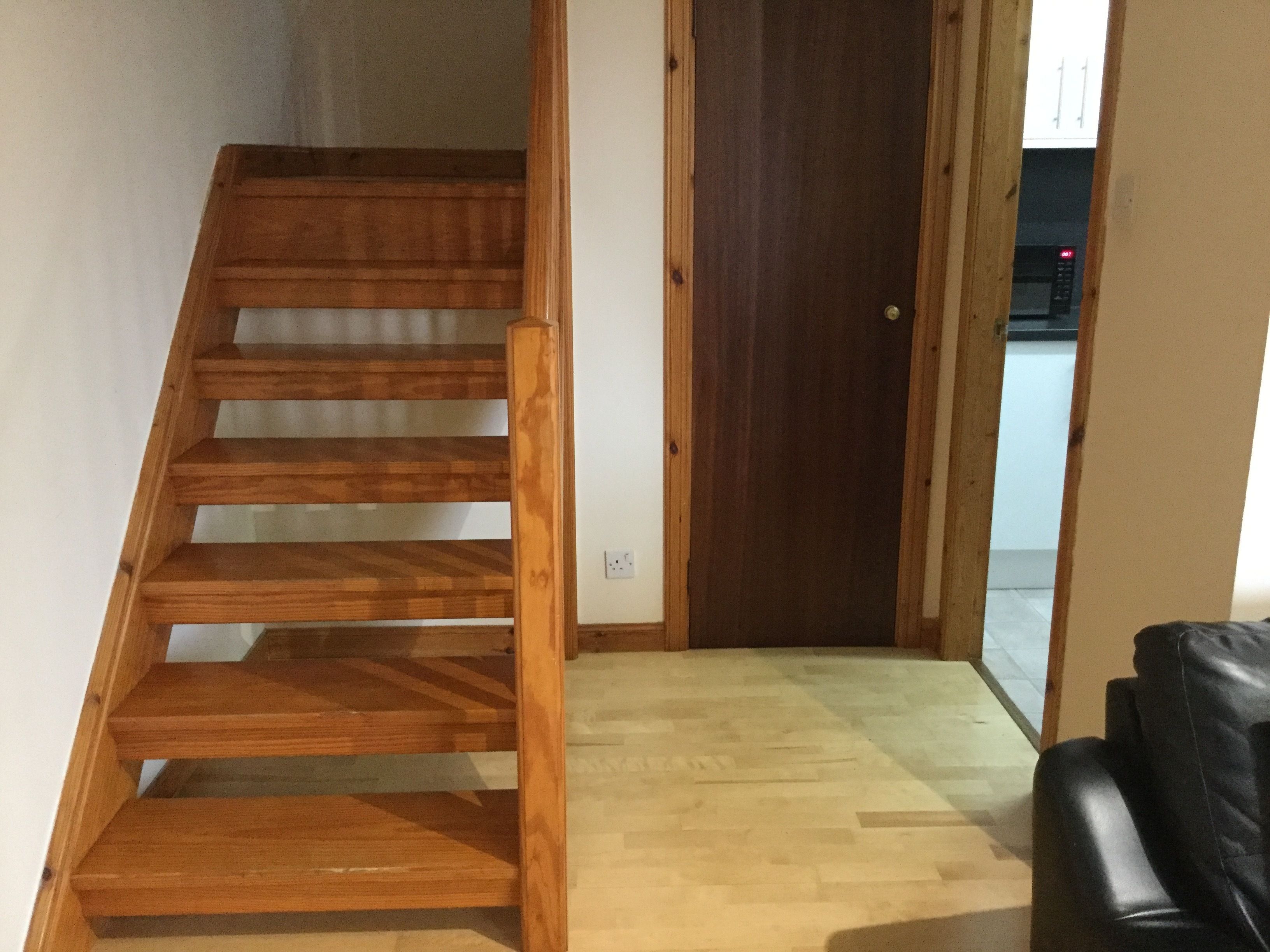 Eine Holztreppe führt zu einer Tür, ein schwarzer Lederstuhl und ein Holzboden.