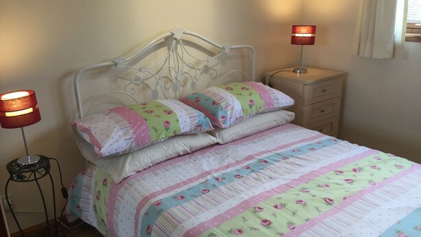 Una cama bien hecha con ropa de cama floral, dos lámparas de noche y una mesita de noche de madera con cajones.