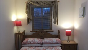 Une chambre à coucher comprenant un lit, deux lampes de chevet, une fenêtre avec des stores, une tête de lit en bois et une table de chevet avec des tiroirs.