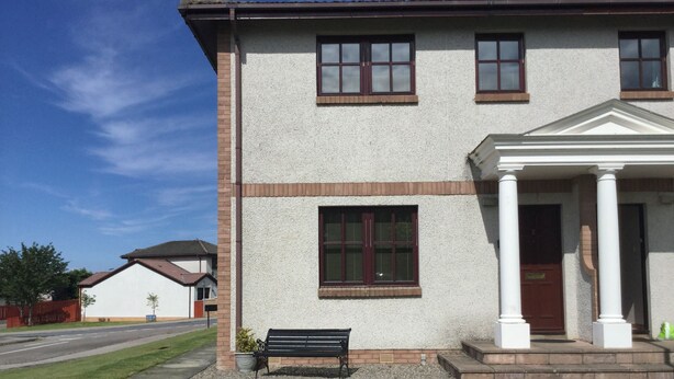 Un bâtiment à deux étages, doté d’une façade blanche, d’un porche à colonnes et d’un banc à l’extérieur.