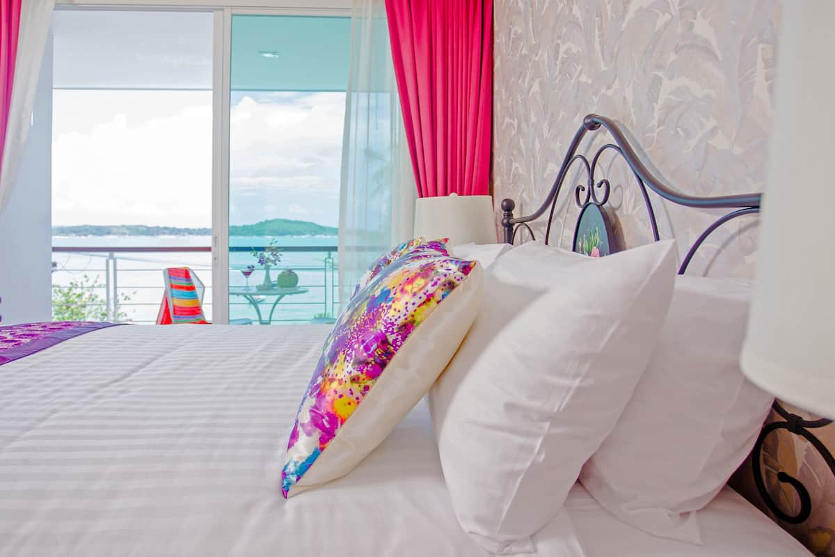 Une chambre avec un lit, une vue sur la mer et un balcon équipé d’une table et de chaises.