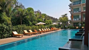 A swimming pool with lounge chairs and umbrellas, surrounded by lush greenery and a building with balconies. - Almali Rawai Beach Residence (Rawai)