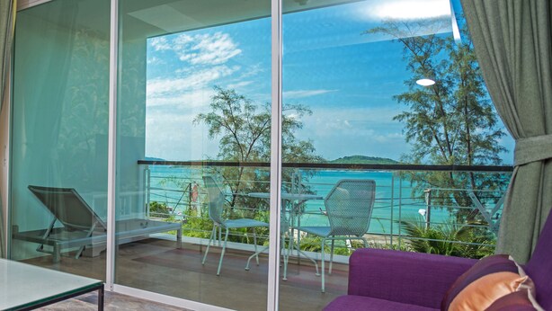 A balcony with a glass door, a purple sofa, and a table with chairs. - Almali Rawai Beach Residence (Rawai)