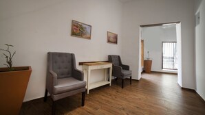 Una habitación con piso de madera, dos sillones grises, una mesa blanca con cajón y dos cuadros en la pared.