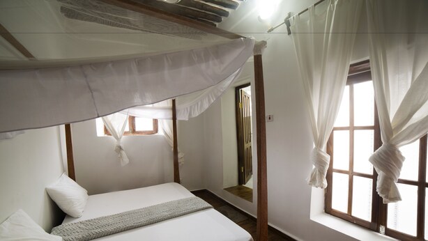 Una cama individual con dosel, ropa de cama blanca y suelo de madera.