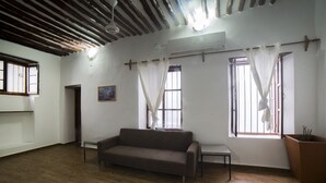 Una habitación amplia con suelo de madera, un sofá, una mesita y un gran ventanal con cortinas.