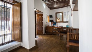 Una habitación con suelo de madera, una puerta grande de madera, un banco, un escritorio y un ventilador de techo.
