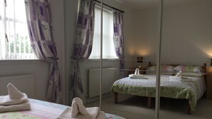 Un dormitorio con dos camas, un radiador y una ventana con cortinas moradas.