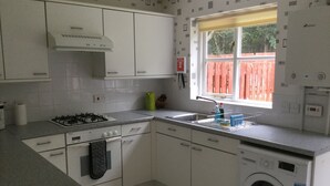 Una cocina compacta con muebles blancos, estufa a gas, lavamanos y lavadora integrada.