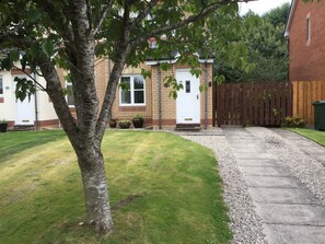 A residential property with a well-maintained lawn, a wooden fence, and a paved driveway leading to a white door. - Inverness Apartments - Castle Heather (Inverness)