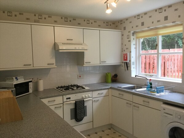 A kitchen with white cabinets, a gas stove, a sink, and a washing machine. - Inverness Apartments - Castle Heather (Inverness)