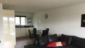 A modern living room with a black leather sofa, a glass coffee table, and a dining area with a black table and chairs. - Inverness Apartments - Castlefield (Inverness)