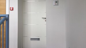 A white door with a number plate '13', a red emergency light, and a small intercom unit. - Inverness Apartments - Castlefield (Inverness)