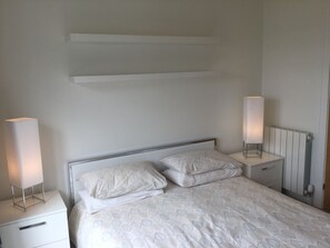 Una cama bien hecha con un edredón estampado, dos mesitas de noche con lámparas y un radiador en la pared.