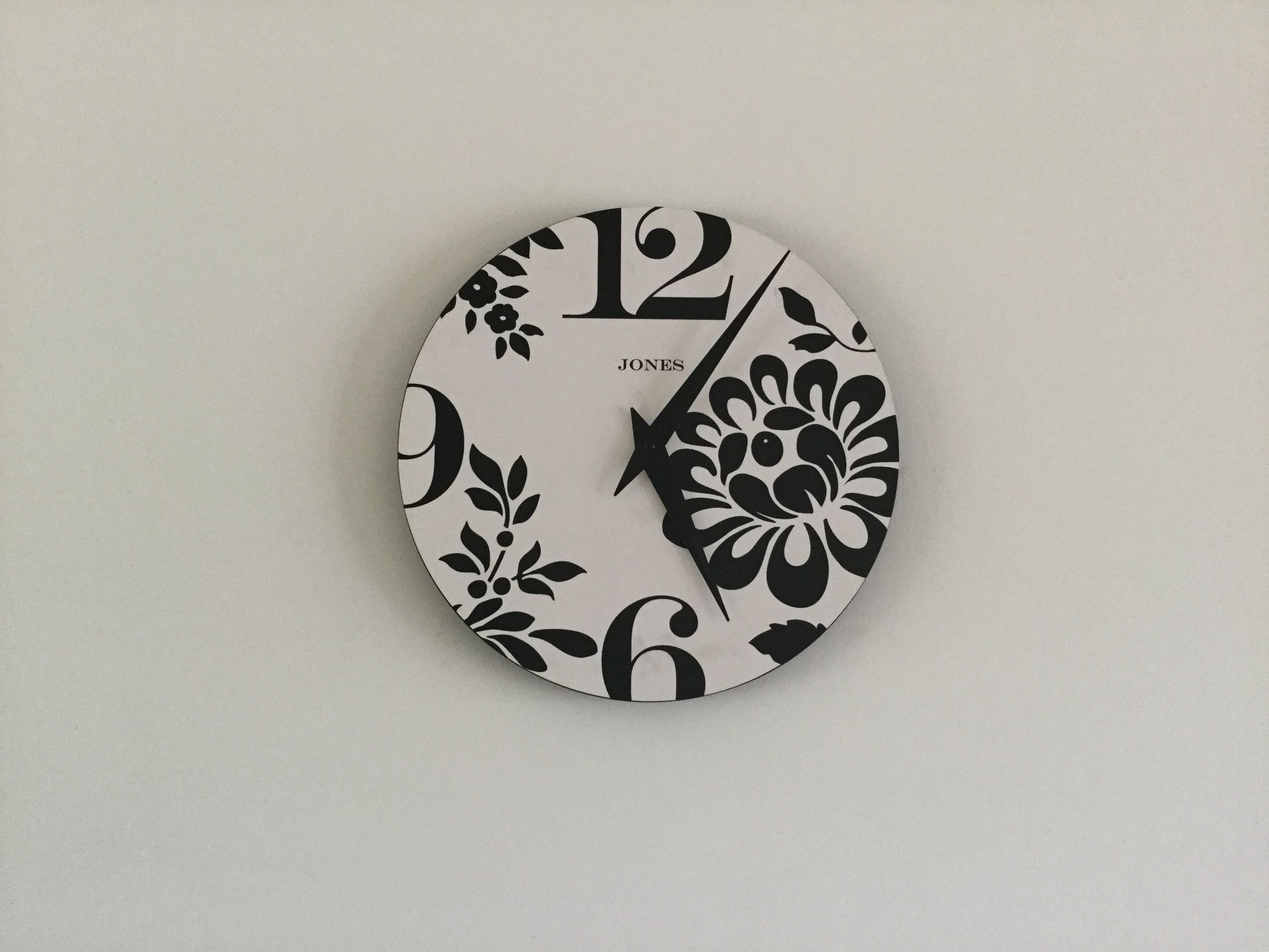 Une horloge murale ronde, ornée d’un motif floral et portant le nom de la marque « JONES ».