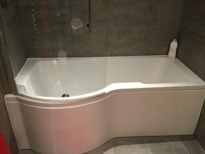 A corner bathtub with a glass enclosure, a white faucet, and a single bottle of shampoo on the right side. - Inverness Apartments - Castlefield (Inverness)